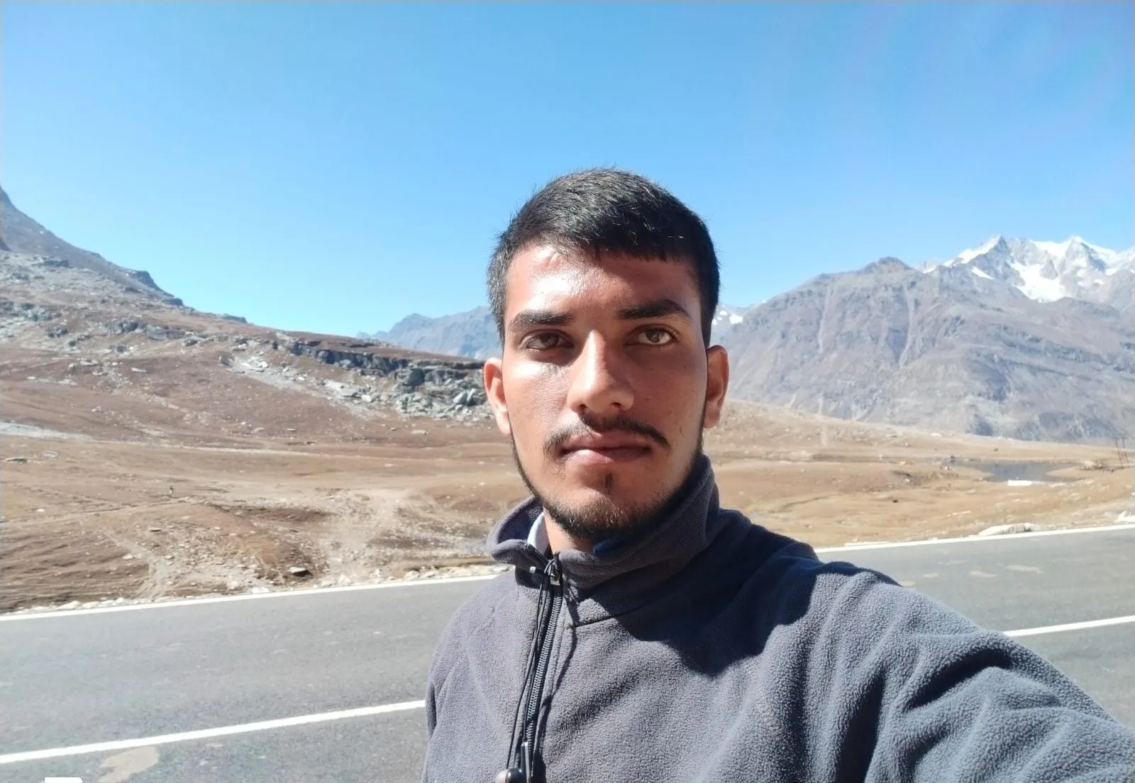 Kulwant on the road near Rohtang Pass, snow-capped peaks behind him