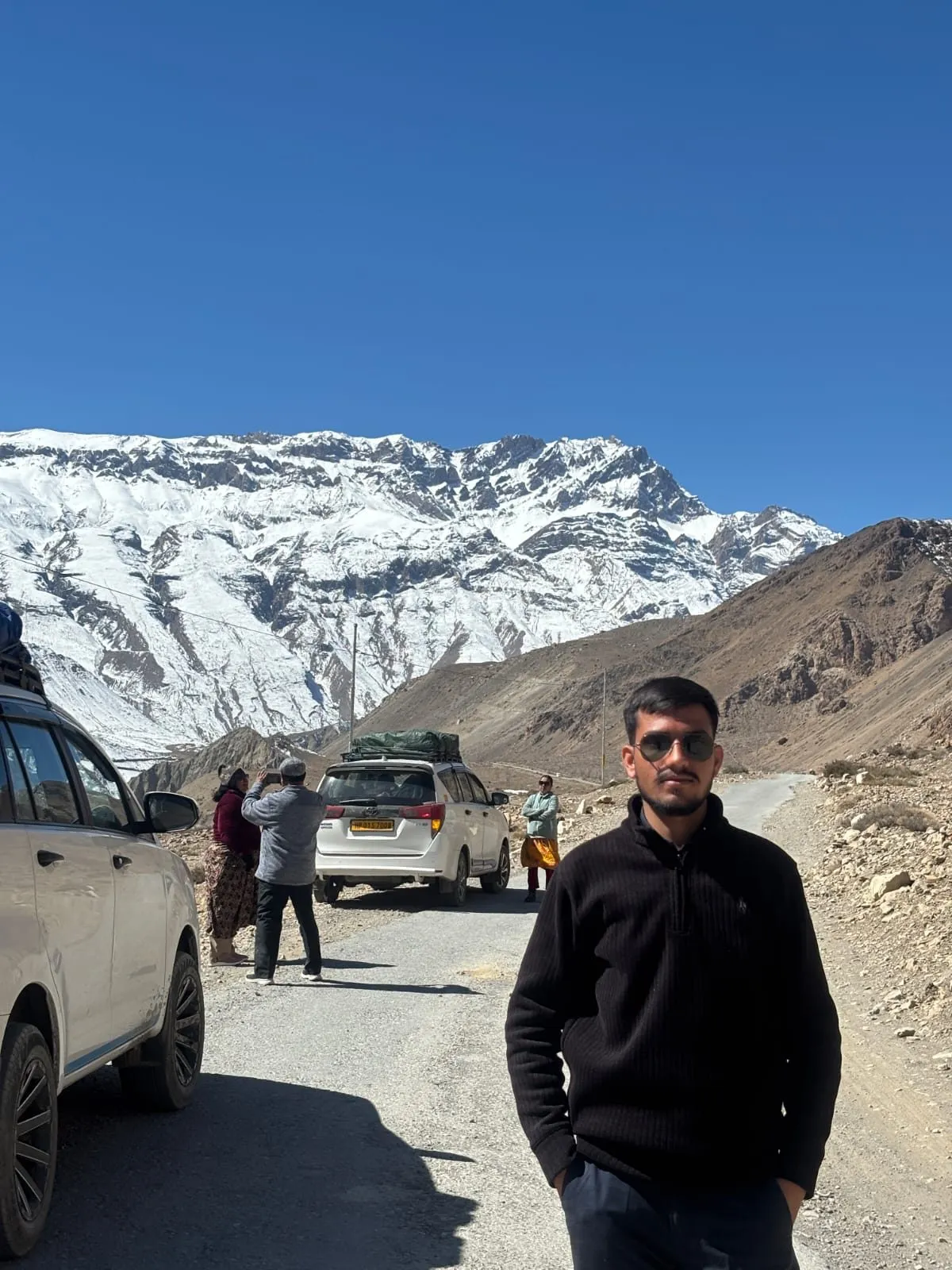 Kulwant standing roadside at Kunzum La, snow-capped peaks behind him