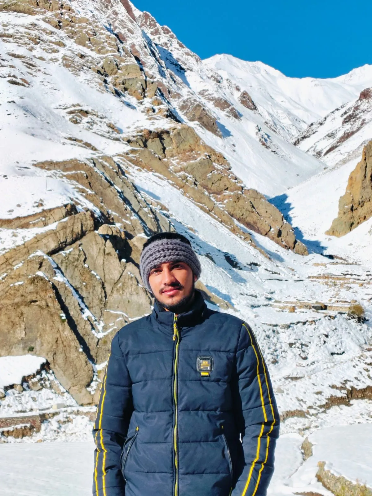 Kulwant standing in front of a snow-covered rocky mountainside near Komic, the world's highest motorable village