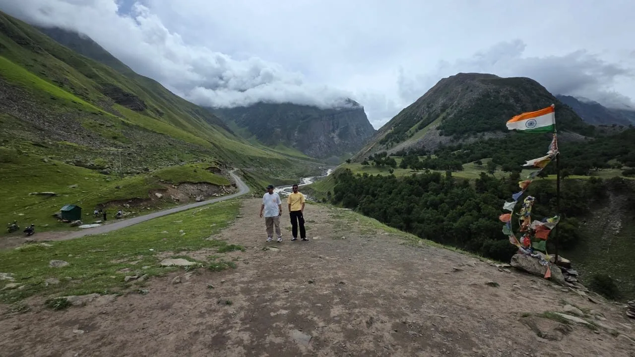 Travelers overlooking the green valley near Chitkul, prayer flags nearby