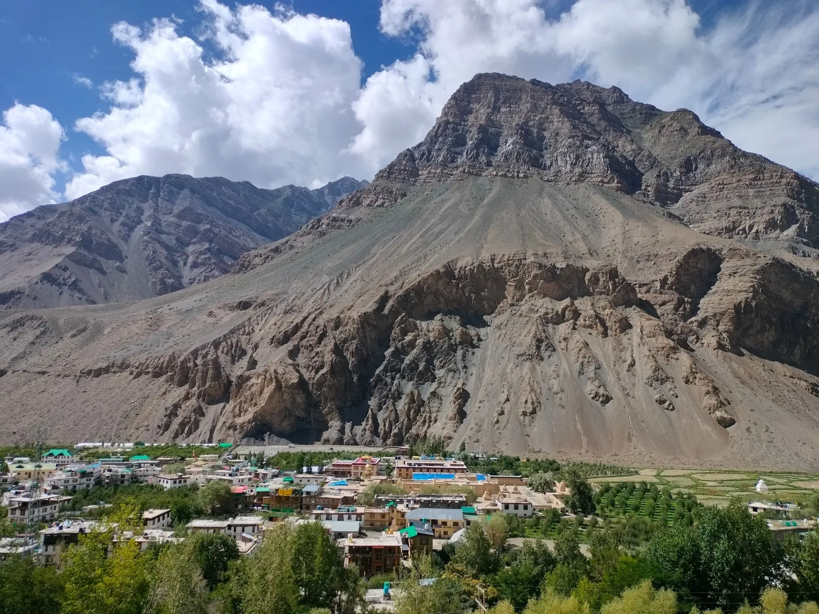 A village nestled in a green valley beneath a large mountain